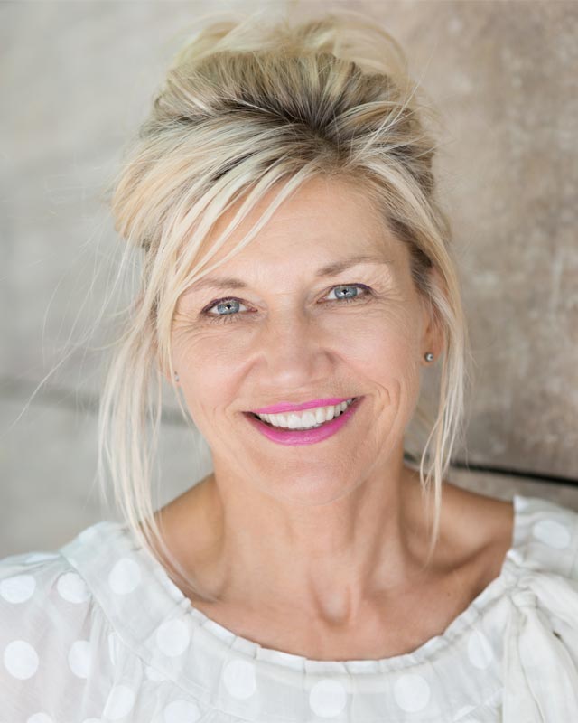 An older woman in a white, polka dot shirt smiling with whitened teeth
