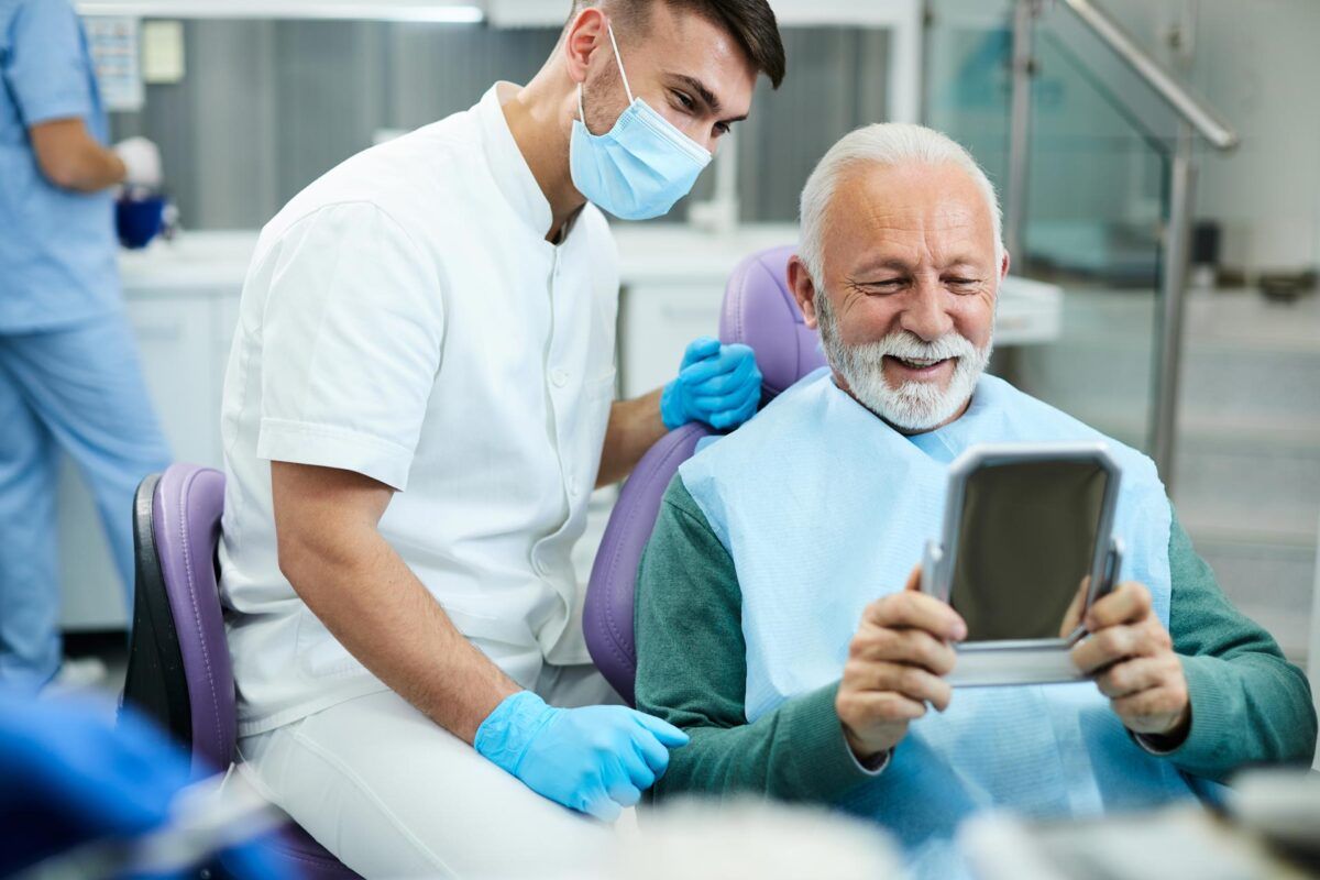 Senior patient and dentist smiling over a hand mirror