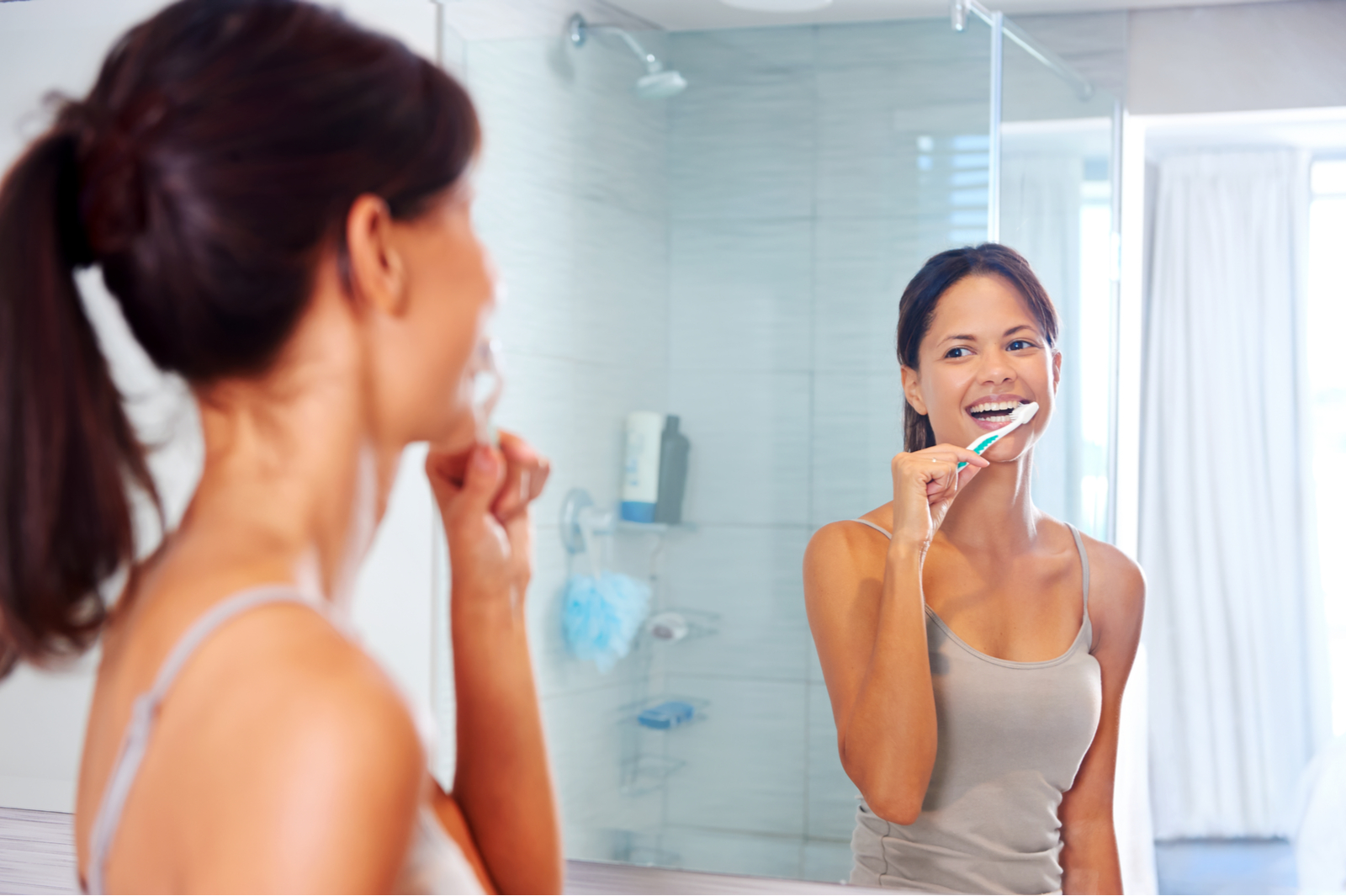 A woman smiling in the mirror while brushing her teeth
