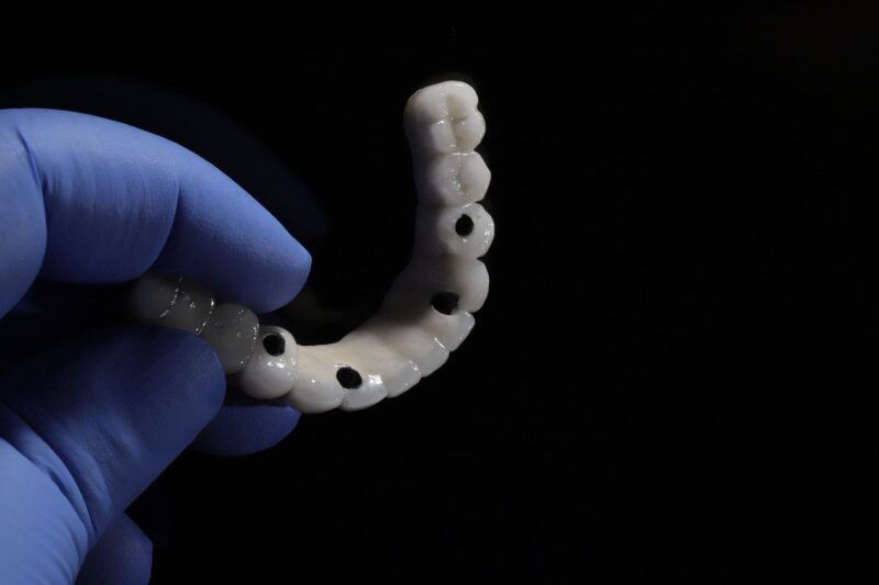 Gloved hand holding a full arch dental bridge for implants