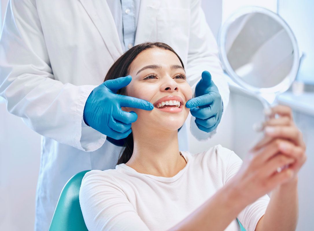 Smiling woman holding a hand mirror while a dentist examines her smile