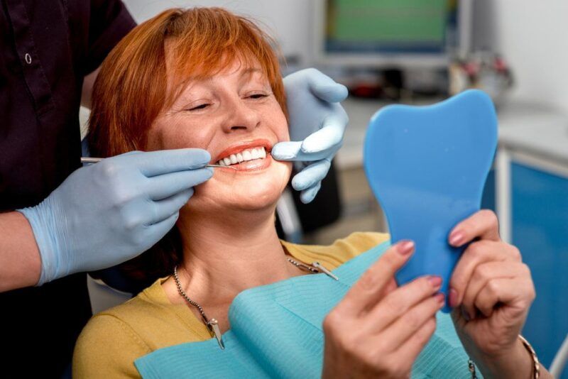 Smiling patient holding a hand mirror in a dental chair