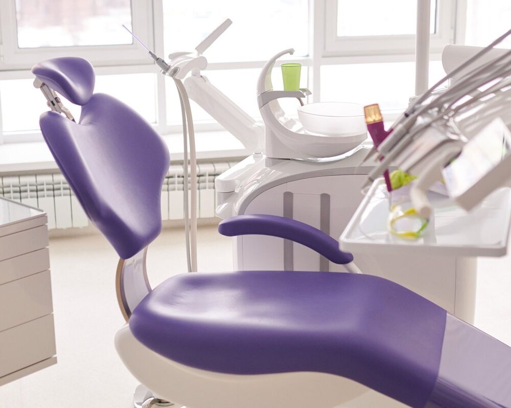 Bright dental treatment room with a purple exam chair